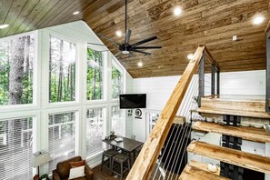 Amplia habitación con ventanas grandes, ventilador de techo, escalera y comedor.