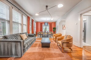Una sala de estar moderna con un sofá gris, un sillón marrón, una mesa de comedor y un ventanal con persianas.