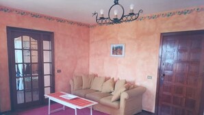 A room with a beige sofa, a red rug, a white table, and a wooden door. - Ciclamino House: Pool, view, wifi, lucca, Tuscany (San Gennaro)