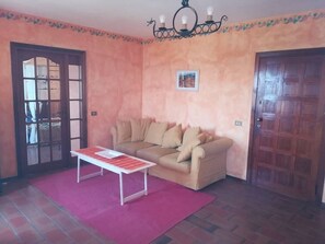 A room with a beige sofa, a red rug, a white table, and a wooden door. - Ciclamino House: Pool, view, wifi, lucca, Tuscany (San Gennaro)