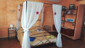 A room with a four-poster bed, a small bedside table, a nightstand, a shelf with books, and a wall-mounted shelf with decorative items. - Ciclamino House: Pool, view, wifi, lucca, Tuscany (San Gennaro)