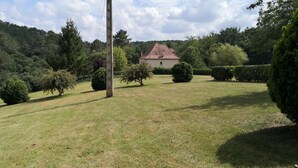Ett lantligt landskap med ett hus, en gräsklädd åker och en skogbeklädd kulle.
