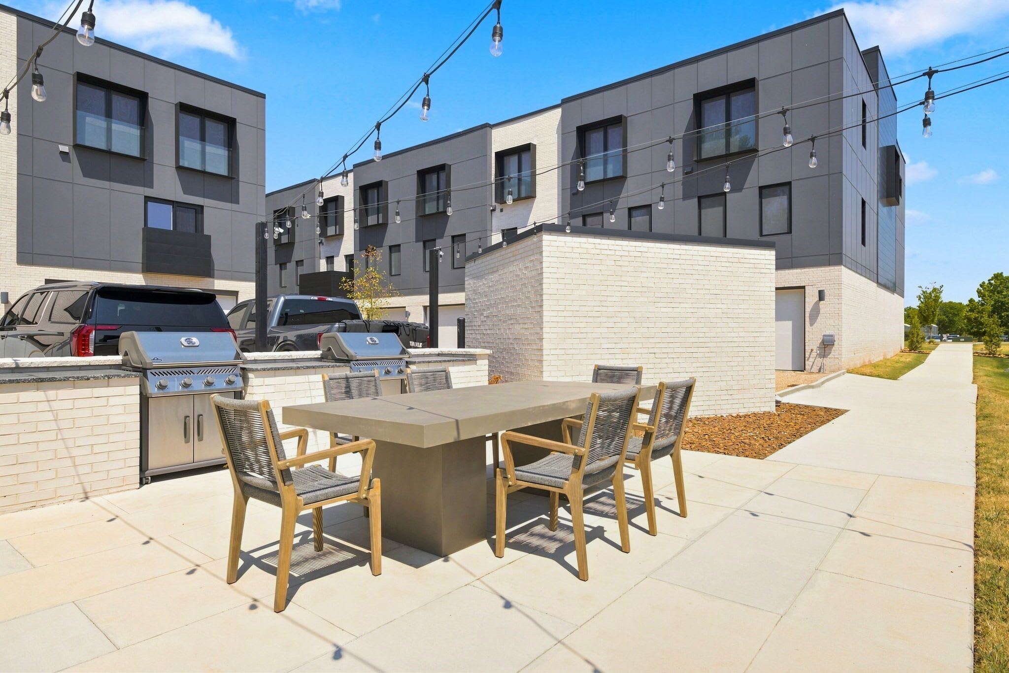 An outdoor patio with a barbecue grill, seating, and a view of modern apartment buildings.