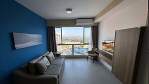 Una habitación de hotel moderna con un ventanal grande, un sofá, una mesita y un televisor.