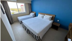 Habitación de hotel con dos camas, una ventana con cortinas, una pared azul y una mesita de noche pequeña.