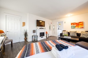 A modern hotel room with a bed, a sofa, a TV, a fireplace, and a dining area. - Downtown Indy Studio apartment (Indianapolis)