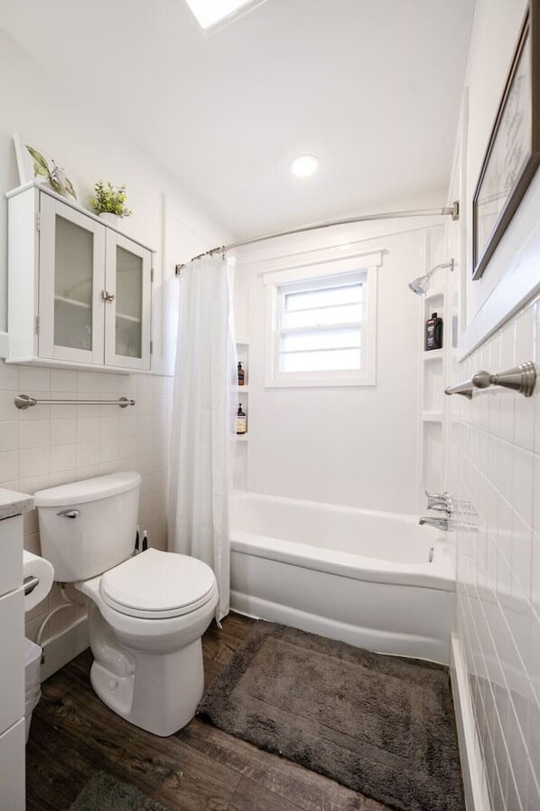 A bathroom with a toilet, a bathtub, a shower curtain, and a window. - Downtown Indy Studio apartment (Indianapolis)