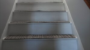 Un escalier avec des marches blanches et des rampes en bois, menant à un palier où se trouvent une petite table et une plante.
