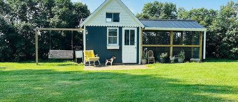 Ein Haus mit überdachter Veranda, einem kleinen Hund und einer Schaukel.