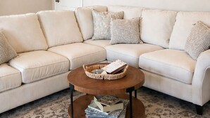 Un salon avec un canapé d’angle beige, une table basse ronde en bois et un élément décoratif mural placé au-dessus du canapé.