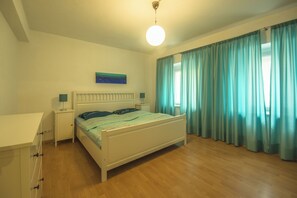 A bedroom with a bed, bedside tables, a nightstand, a ceiling light, a window with curtains, and a wall-mounted artwork. - Haus Spiegel - Holiday apartment Mediterran 2 (Lindau (Bodensee))