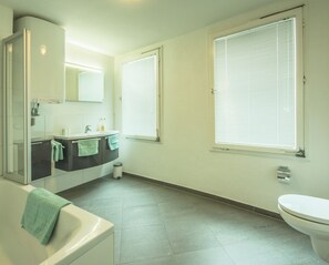 A bathroom with a bathtub, toilet, sink, and two windows with blinds. - Haus Spiegel - Holiday apartment Mediterran 2 (Lindau (Bodensee))