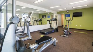 A gym with exercise equipment, a treadmill, and a mirror. - Everstay Living Extended Stay (Plano)