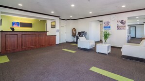 A reception area with a wooden desk, a reception counter, and a seating area with white sofas. - Everstay Living Extended Stay (Plano)