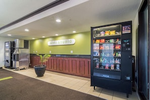 A kitchenette area with a coffee machine, a large potted plant, and a vending machine labeled 'PUSH'. - Everstay Living Extended Stay (Plano)
