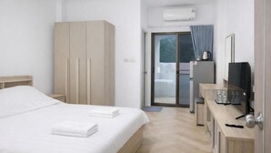 A hotel room with a bed, wardrobe, desk, television, and a sliding door leading to a balcony.