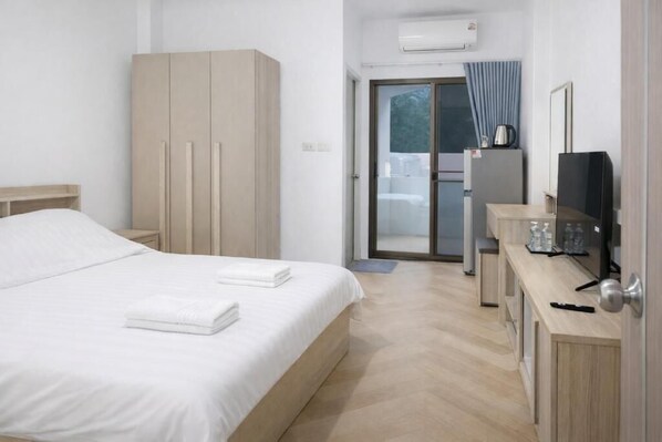 Ein Hotelzimmer mit Bett, Kleiderschrank, Schreibtisch, Fernseher und einer Schiebetür zum Balkon.