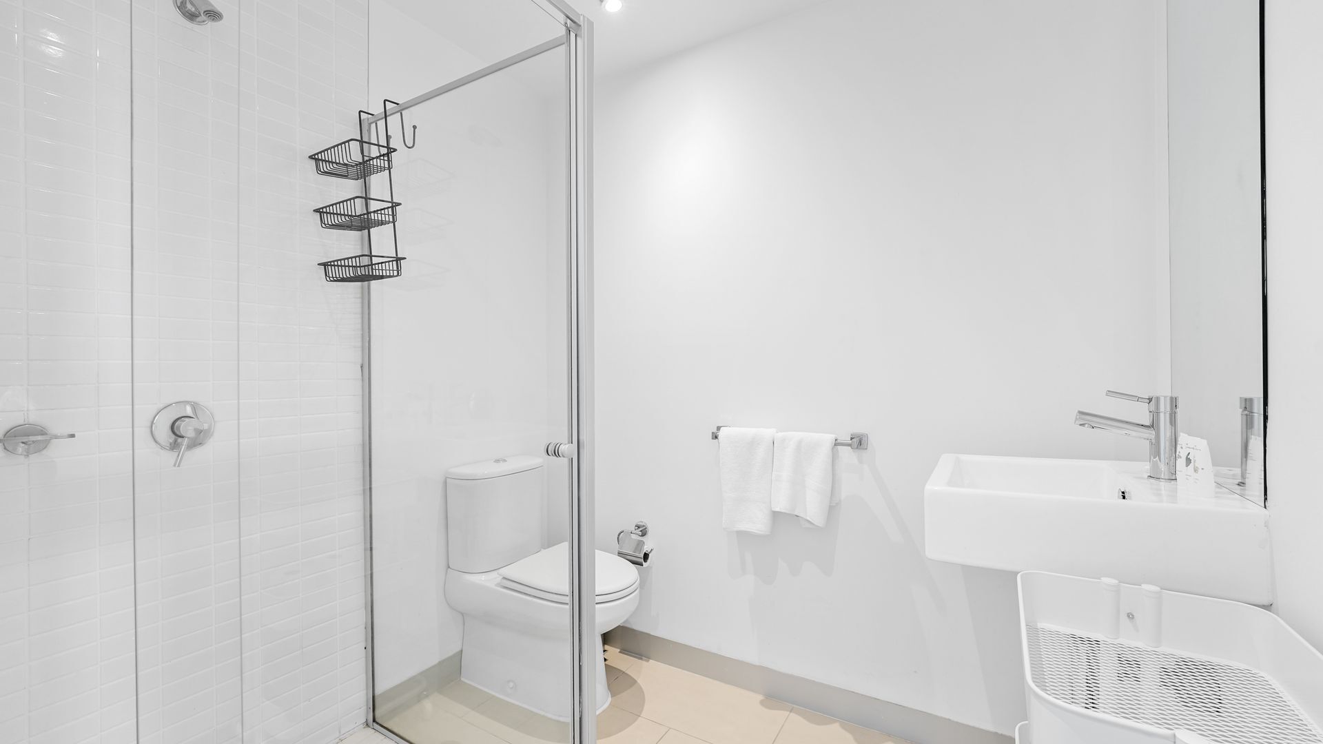 A modern bathroom with a glass shower enclosure, a toilet, a sink, and a towel rack.