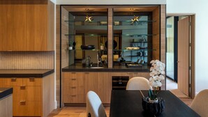 A modern kitchen with wooden cabinets, a glass backsplash, and a dining area with a black table and chairs. - Modern Luxury in Downtown Ketchum (Ketchum)