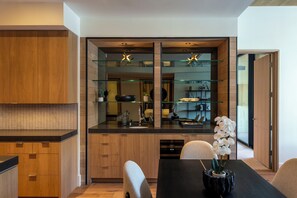 A modern kitchen with wooden cabinets, a glass backsplash, and a dining area with a black table and chairs. - Modern Luxury in Downtown Ketchum (Ketchum)