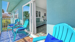 A balcony with turquoise chairs, a patterned rug, and a view of a green lawn and palm trees. - INCREDIBLE! Oceanfront Dream Escape! Unit 21 is a Rare 3-Bedroom Condo! (Cocoa Beach)