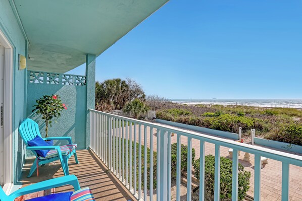 A balcony with two turquoise chairs, a potted plant, and a view of the beach and ocean.