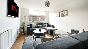 En moderne stue med et stort fladskærms-tv, en grå sofa, et sofabord og en potteplante.