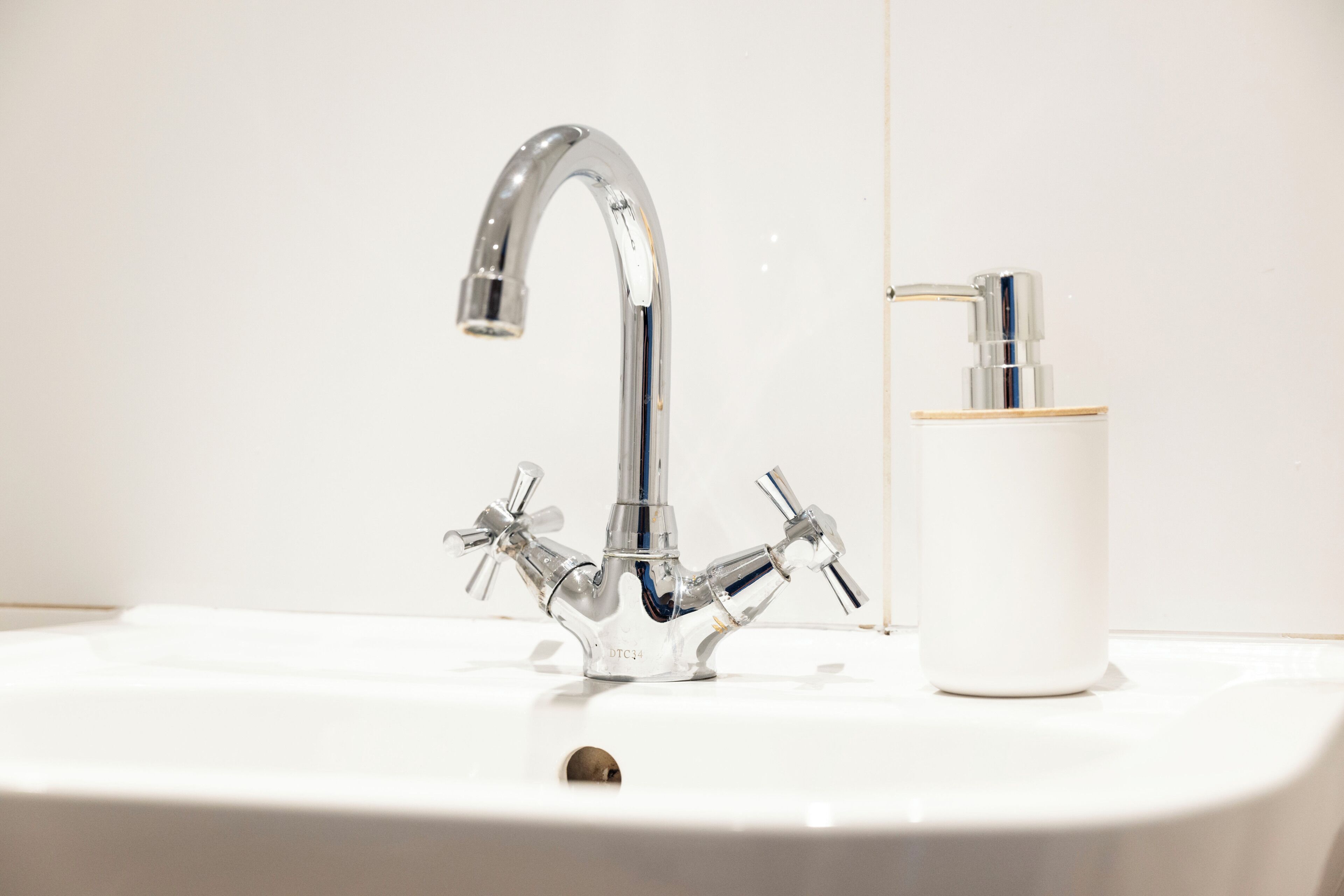 Ein Badezimmer mit einem Chrom-Wasserhahn, einer Seifenspender und einem weißen Waschbecken.