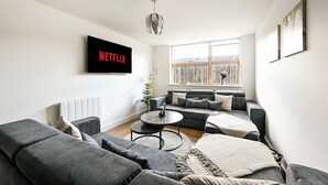 En moderne stue med en grå sofa, et sofabord og et fjernsyn, der viser 'NETFLIX'.