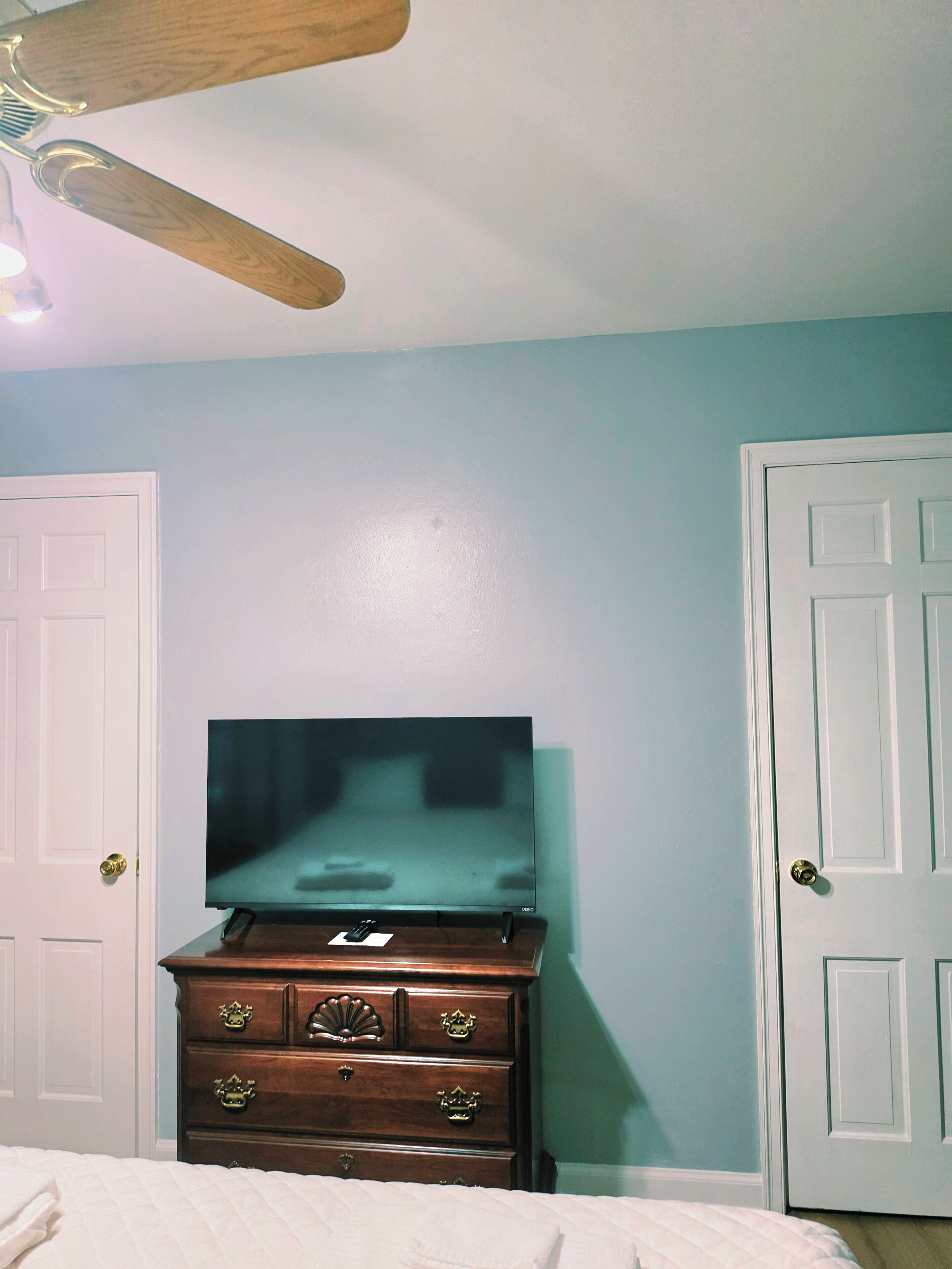 A bedroom with a bed, a dresser, a television, and a ceiling fan.