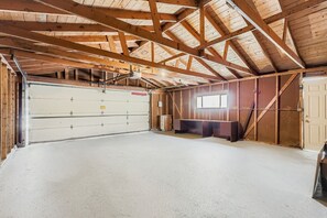 A spacious garage with a concrete floor, wooden beams, a large garage door, and a window.