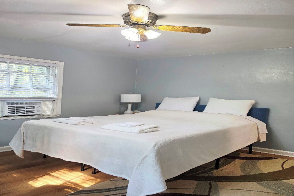 A bedroom with a bed, a ceiling fan, a window with blinds, and a wall-mounted air conditioning unit.