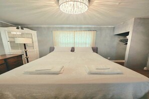 A hotel room with a large bed, a chandelier, a window with curtains, and a desk with a lamp. -  Great for Groups &Families, Sleeps 9, Fenced yard,BBQ, Garage Parking,Discounts (Milwaukee)