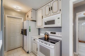 Una cocina con muebles blancos, un refrigerador, un microondas, un horno y una tetera.