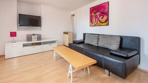 Ett modernt vardagsrum med en soffa, en träbänk, en platt-TV, ett element och en färgstark, abstrakt tavla.