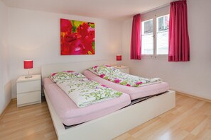 A bedroom with a bed, bedside tables, a window with curtains, and a colorful painting on the wall. - Haus Spiegel - Holiday apartment with roof terrace - Mediterran 3 (Lindau (Bodensee))