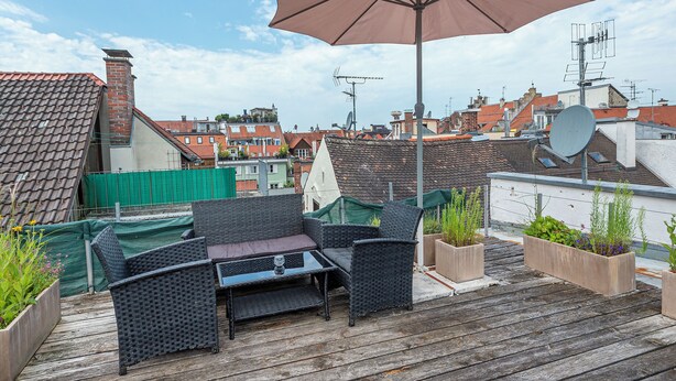 En takterrass med utemöbler, ett stort parasoll och krukväxter.