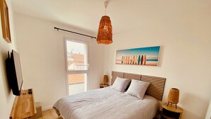 Ett sovrum med en säng, en hängande lampa, en tavla, en tv och ett fönster.
