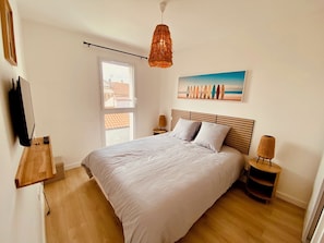 Ein Schlafzimmer mit Bett, einer Pendelleuchte, einem Gemälde, einem Fernseher und einem Fenster.