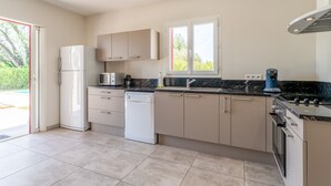 A modern kitchen with a dishwasher, oven, and a window overlooking greenery. - Holiday Home 'Les Cinsault' with Private Pool, Wi-Fi and Air Conditioning (Vaison-la-Romaine)