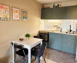 Une cuisine compacte avec une table et des chaises blanches, une petite plante en pot et un four à micro-ondes.