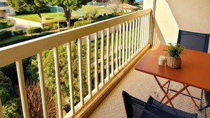 Un balcon avec une table et des chaises, une vue sur un court de tennis et un bâtiment en arrière-plan.