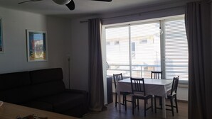 Ein Wohnzimmer mit einer Couch, einem Esstisch mit Stühlen, einem Deckenventilator und einem Fenster mit Jalousien.