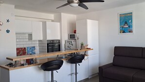 Eine moderne Küche mit weißen Schränken, einer Holzauskładung und zwei schwarzen Barhocker. Es gibt ein dunkelbraunes Sofa und zwei gerahmte Poster an der Wand.