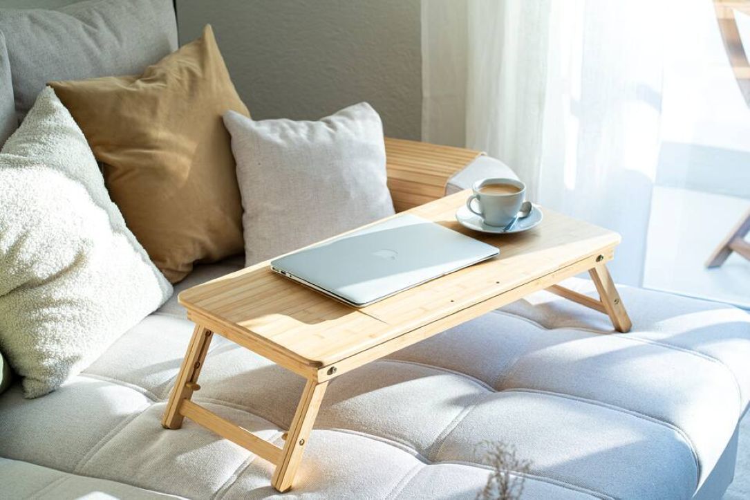 Un portatile su un tavolo di legno, una tazza di caffè e un divano con cuscini.