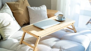 A laptop on a wooden table, a cup of coffee, and a sofa with cushions.