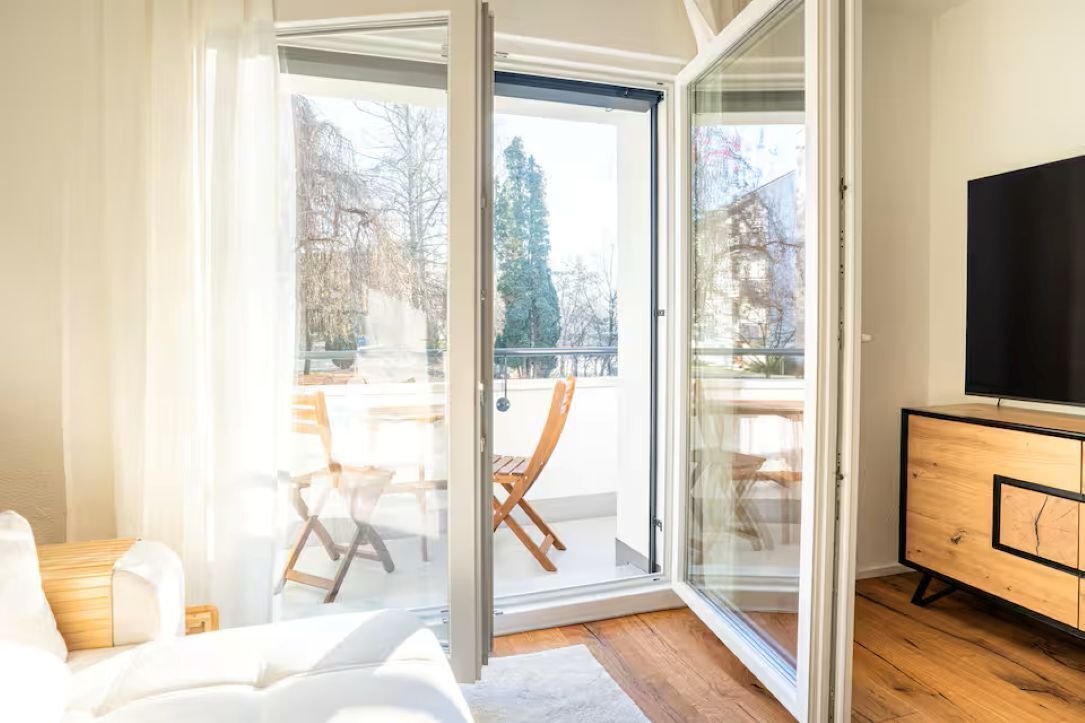 Uma sala de estar moderna com uma porta de vidro deslizante que dá para uma varanda, uma televisão de tela plana e um armário de madeira.