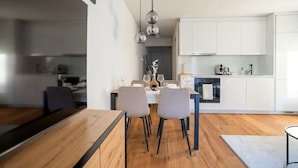 A modern kitchen with white cabinets, a dining area with a wooden table and chairs, and pendant lighting.