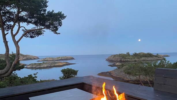 Eine Terrasse mit Feuerstelle, mit Blick auf eine Küstenlandschaft mit Felsformationen und ruhigem Wasser.