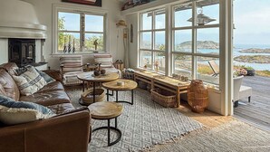 Ein gemütliches Wohnzimmer mit Kamin, großen Fenstern, einer Holterrasse und Meerblick.